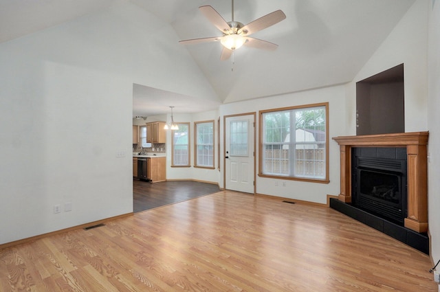 unfurnished living room with visible vents, high vaulted ceiling, dark wood-type flooring, a fireplace with raised hearth, and ceiling fan with notable chandelier