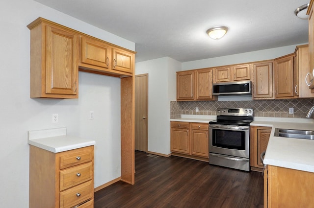 kitchen featuring dark wood-type flooring, light countertops, tasteful backsplash, a sink, and appliances with stainless steel finishes