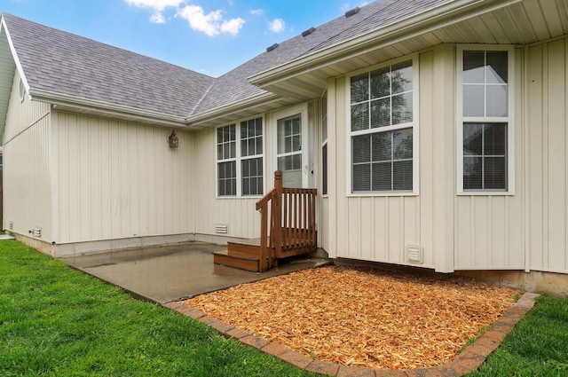 doorway to property with a lawn, a patio, and a shingled roof