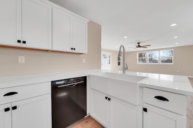 kitchen featuring a sink, light countertops, black dishwasher, a peninsula, and white cabinetry
