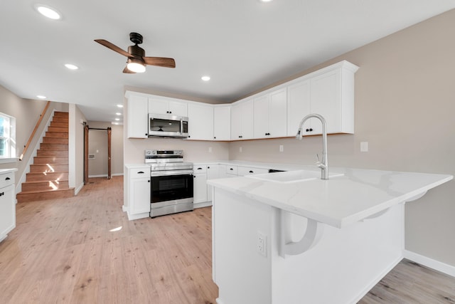 kitchen with a peninsula, ceiling fan, a sink, light wood finished floors, and appliances with stainless steel finishes
