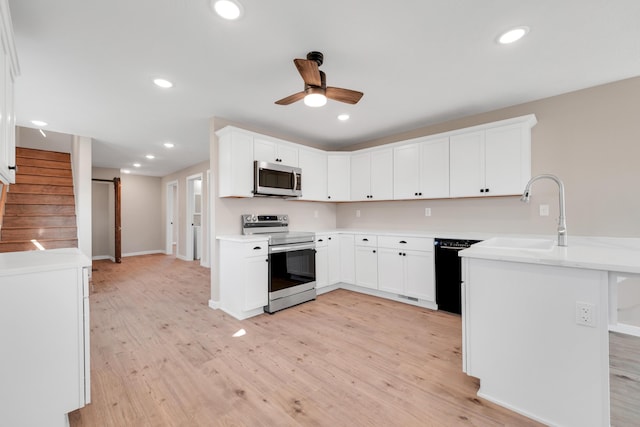 kitchen with a sink, a peninsula, a ceiling fan, light wood finished floors, and appliances with stainless steel finishes