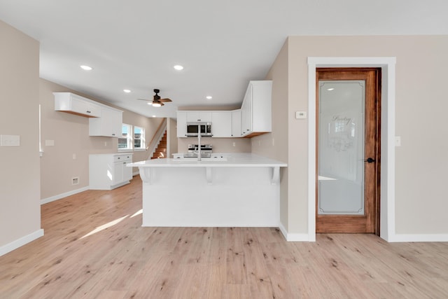 kitchen with a peninsula, baseboards, light wood-type flooring, light countertops, and appliances with stainless steel finishes