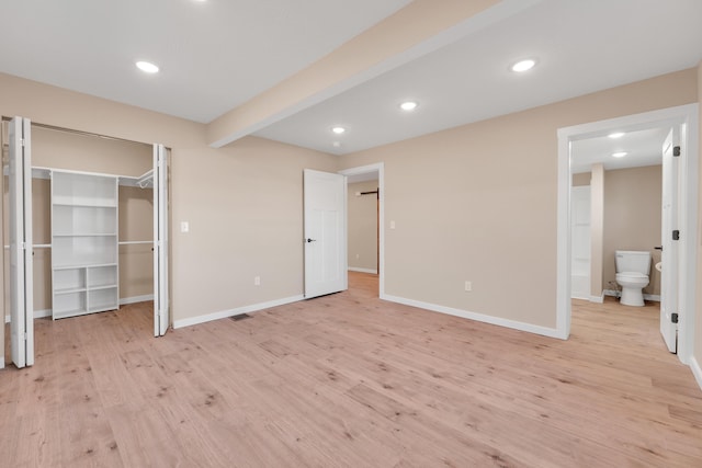unfurnished bedroom with light wood-style floors, baseboards, ensuite bathroom, and a spacious closet