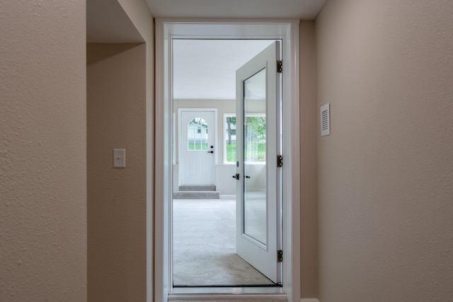 doorway to outside featuring a textured wall and carpet