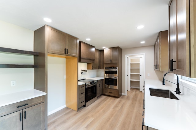 kitchen with open shelves, a sink, light countertops, light wood-style flooring, and stainless steel appliances