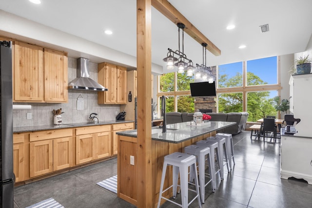 kitchen with tasteful backsplash, a sink, wall chimney exhaust hood, a kitchen bar, and visible vents