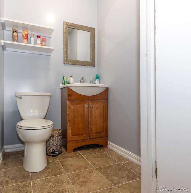 half bath featuring baseboards, tile patterned flooring, vanity, and toilet