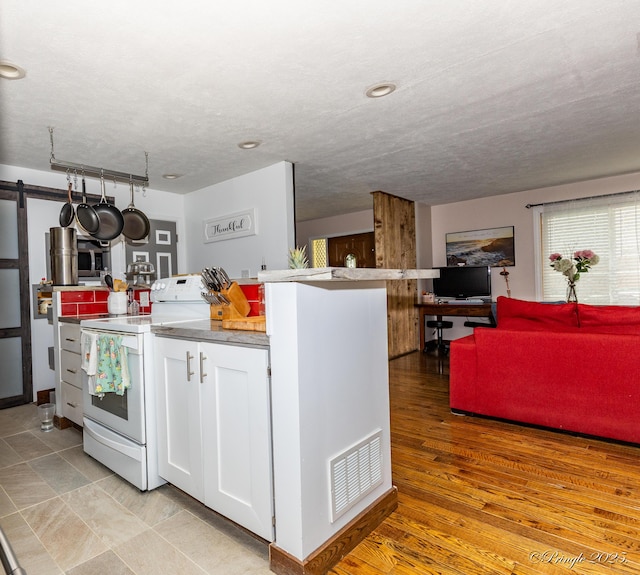kitchen featuring white range with electric stovetop, white cabinets, visible vents, and a barn door