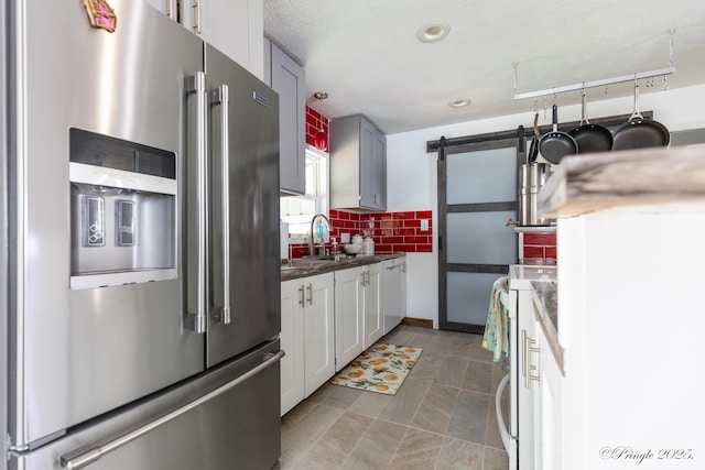 kitchen with a barn door, stove, decorative backsplash, stainless steel refrigerator with ice dispenser, and dark countertops