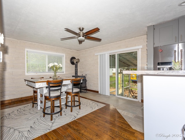 dining area featuring baseboards, a wood stove, ceiling fan, and wood finished floors