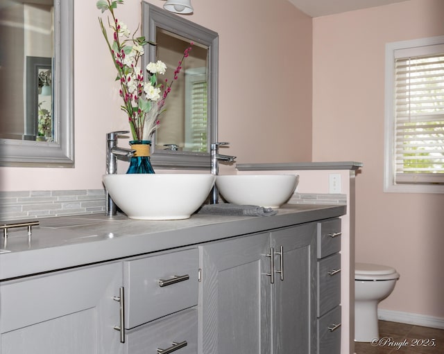 bathroom featuring double vanity, toilet, baseboards, and a sink