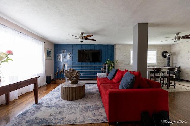 living area featuring a wood stove, a textured ceiling, a ceiling fan, and wood finished floors