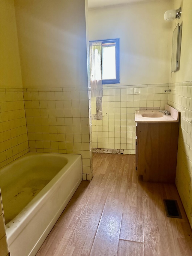 bathroom featuring visible vents, vanity, wood finished floors, tile walls, and a bath