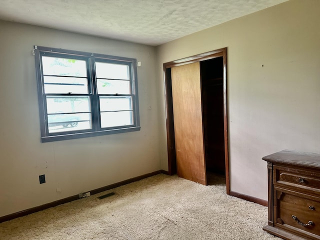 unfurnished bedroom with a textured ceiling, visible vents, baseboards, a closet, and light carpet