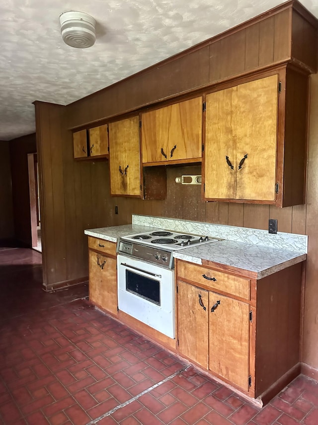 kitchen with light countertops, white electric stove, a textured ceiling, and brown cabinets