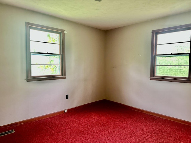 spare room with visible vents, baseboards, and dark colored carpet