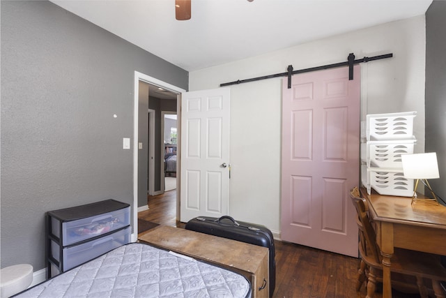 bedroom with baseboards, a barn door, ceiling fan, and wood finished floors