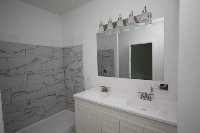 bathroom featuring double vanity, tiled shower, and a sink