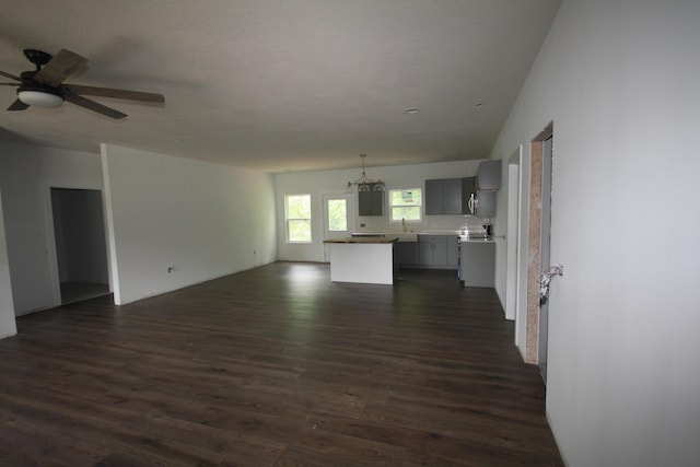 unfurnished living room featuring a sink, dark wood-style flooring, and ceiling fan with notable chandelier