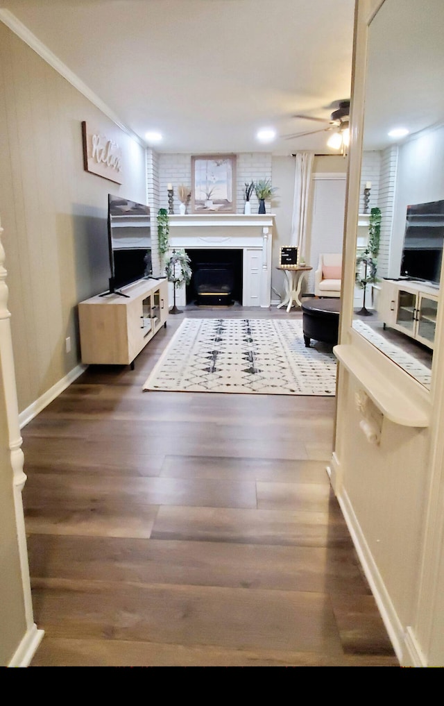 living room with ceiling fan, crown molding, a fireplace, wood finished floors, and baseboards