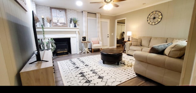 living area featuring crown molding, a ceiling fan, a glass covered fireplace, and wood finished floors