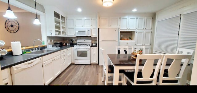 kitchen with dark countertops, a sink, light wood-style floors, white appliances, and white cabinetry