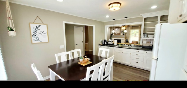 kitchen featuring dark countertops, a fireplace, wood finished floors, a sink, and white appliances