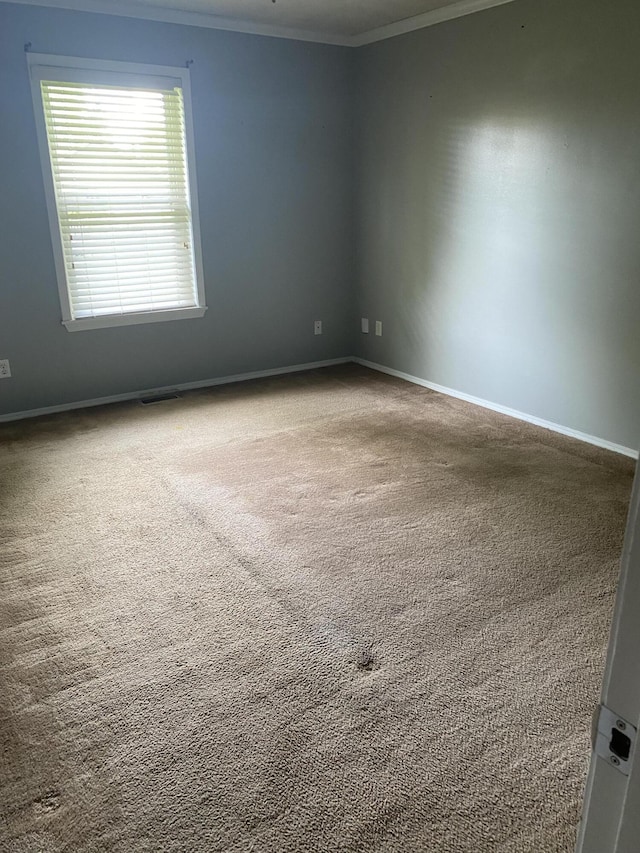 empty room with crown molding, baseboards, carpet floors, and visible vents