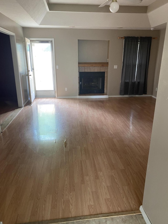 unfurnished living room featuring baseboards, ceiling fan, a tiled fireplace, and wood finished floors
