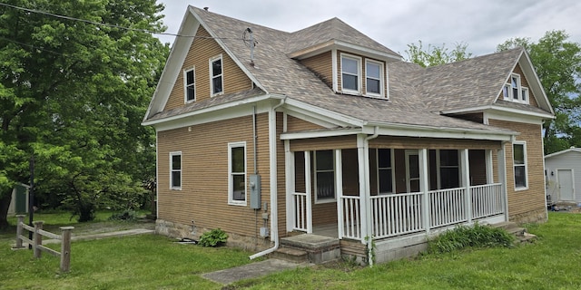 back of house with roof with shingles, covered porch, and a lawn