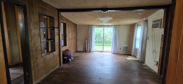 empty room with visible vents, wooden walls, dark wood-type flooring, a textured ceiling, and a wall mounted AC