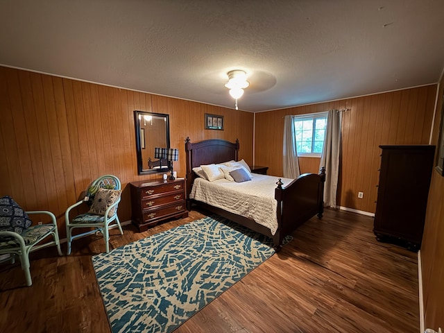 bedroom with wooden walls, a textured ceiling, baseboards, and dark wood-type flooring