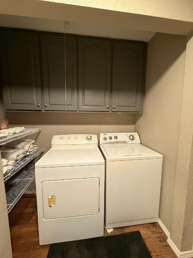 washroom featuring baseboards, cabinet space, washing machine and dryer, and wood finished floors