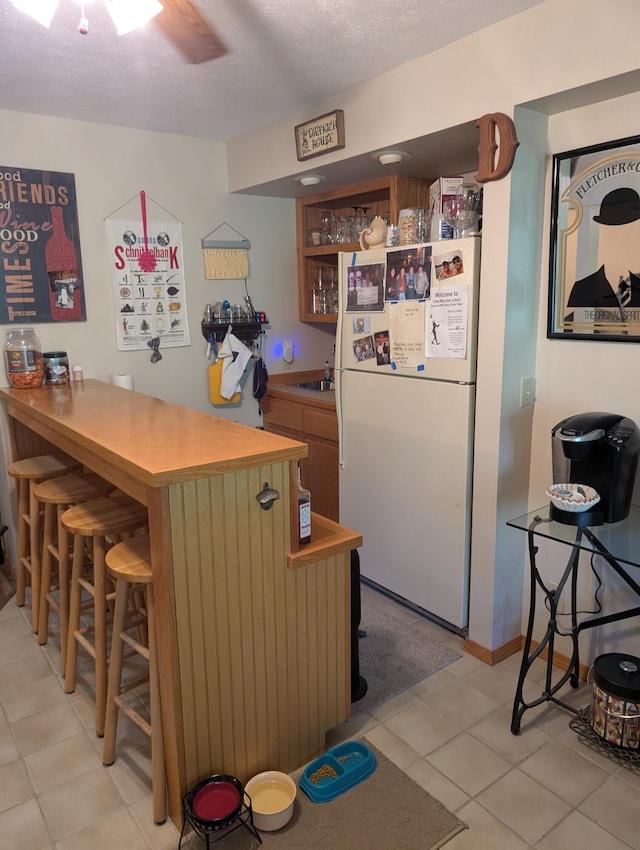 249 Mount Vernon Rd, Forsyth, MO 65653 - kitchen with freestanding refrigerator, a textured ceiling, light tile patterned floors, and a breakfast bar