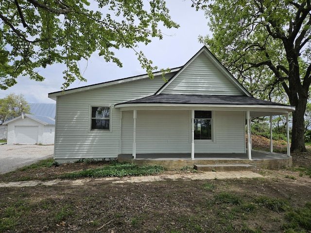 rear view of property featuring a garage, covered porch, an outdoor structure, and a shingled roof