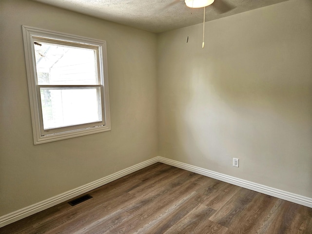 empty room featuring a textured ceiling, baseboards, visible vents, and dark wood-style floors