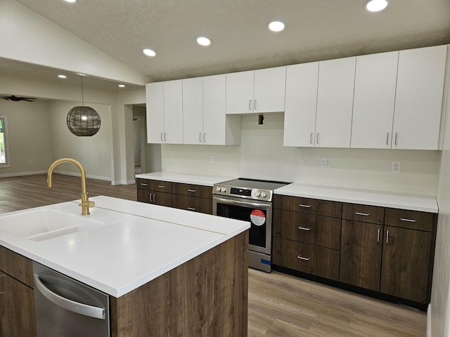 kitchen featuring appliances with stainless steel finishes, a sink, light wood finished floors, lofted ceiling, and white cabinetry