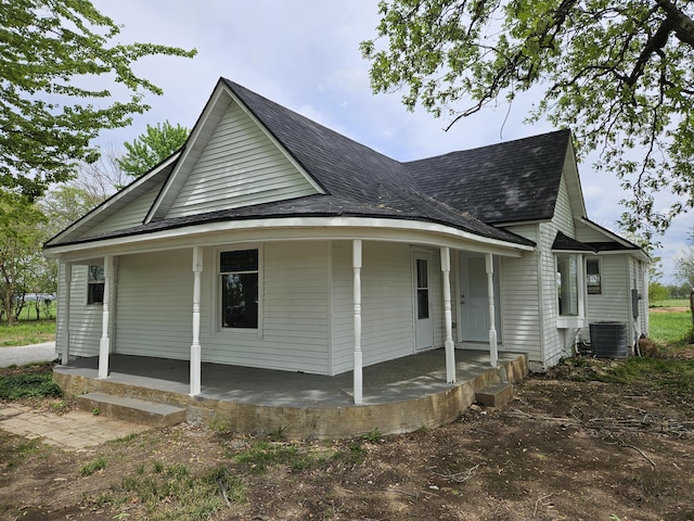 view of front of house with covered porch, a shingled roof, and central AC
