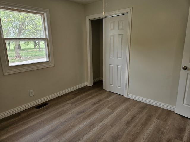 unfurnished bedroom with baseboards, visible vents, dark wood finished floors, and a closet