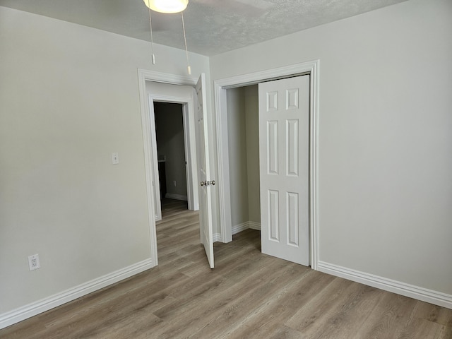 unfurnished bedroom featuring light wood-type flooring, a textured ceiling, baseboards, and a closet