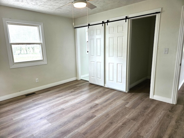 unfurnished bedroom featuring visible vents, wood finished floors, baseboards, a barn door, and a textured ceiling