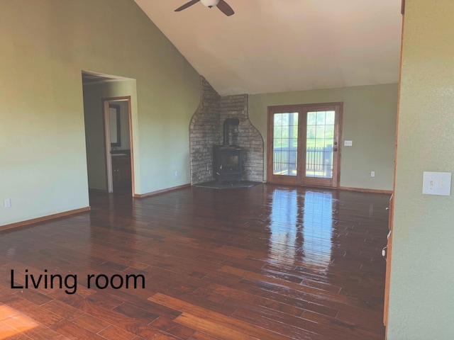 unfurnished living room with wood-type flooring, a wood stove, baseboards, ceiling fan, and high vaulted ceiling