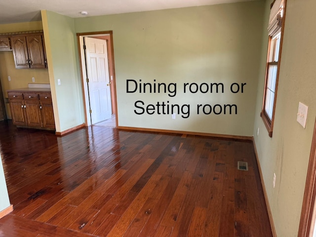 empty room featuring visible vents, dark wood-style flooring, and baseboards