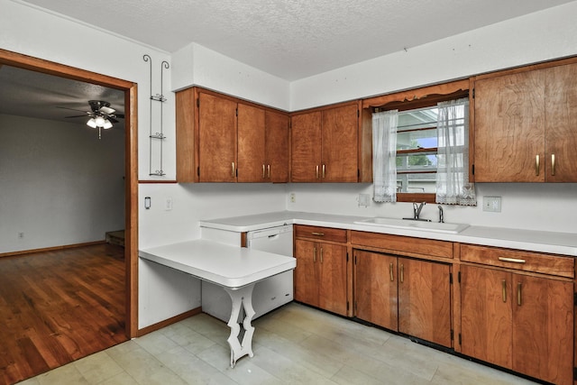 kitchen with ceiling fan, light countertops, a textured ceiling, brown cabinets, and a sink