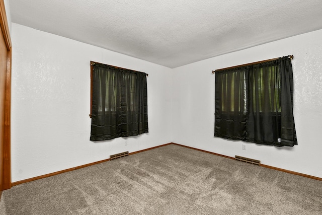 carpeted empty room with visible vents, a textured ceiling, and baseboards