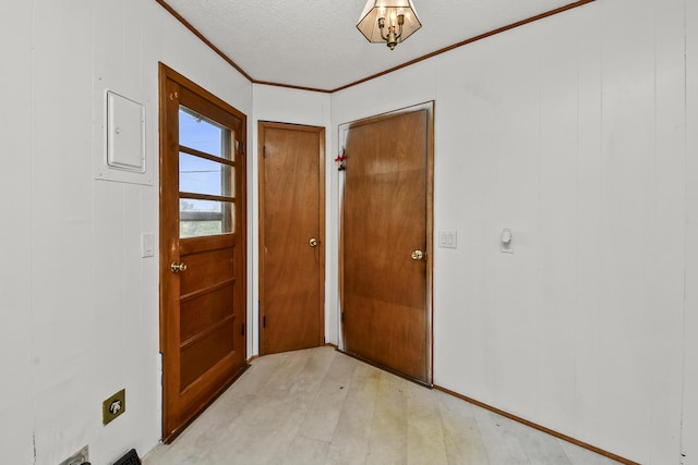 doorway with a textured ceiling, ornamental molding, and light wood-style flooring