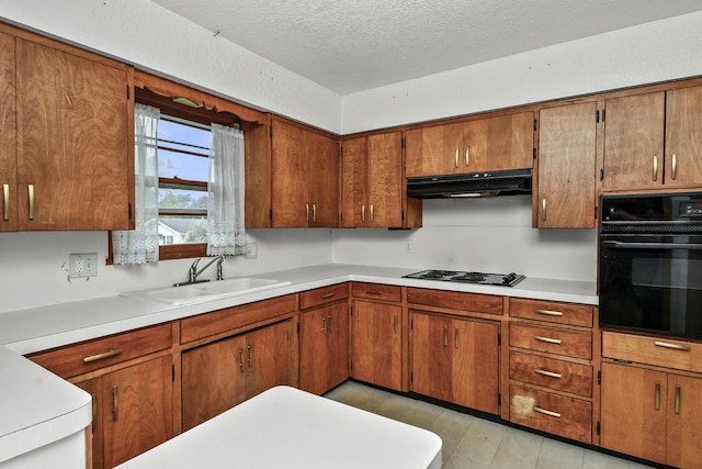 kitchen featuring brown cabinetry, a sink, light countertops, black appliances, and under cabinet range hood