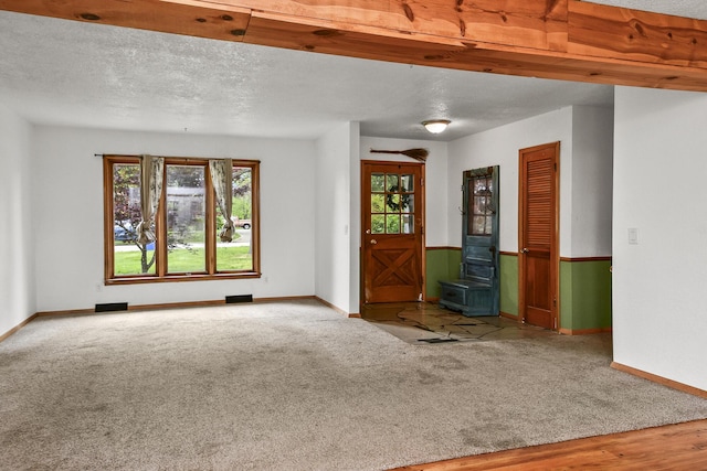 unfurnished living room featuring baseboards, a wood stove, carpet, and a textured ceiling