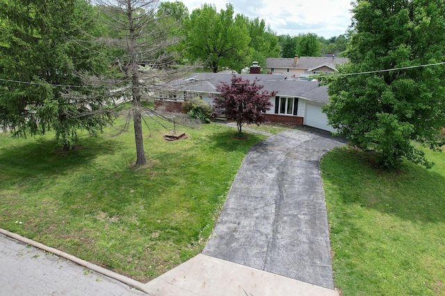 view of front of property featuring aphalt driveway, a chimney, a garage, brick siding, and a front lawn